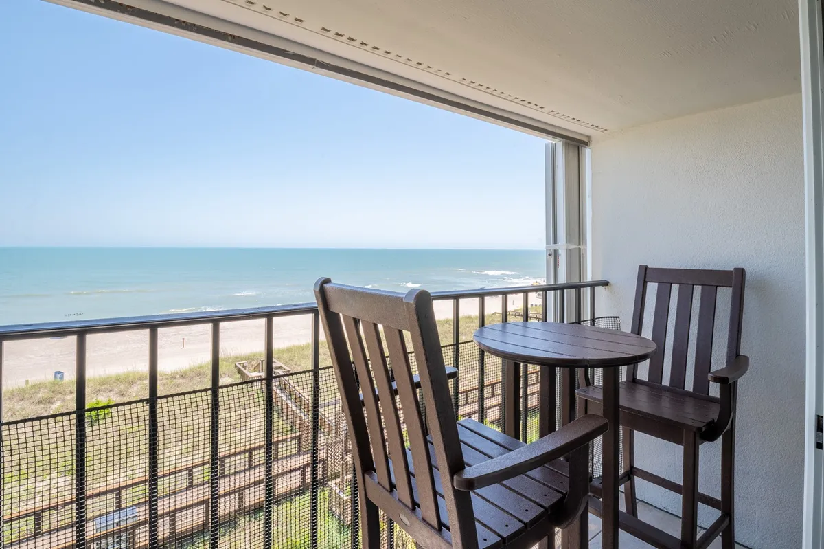 An inviting fourth-floor balcony featuring a sturdy railing, comfortable outdoor seating, and a panoramic view of the Atlantic Ocean. The tranquil setting is ideal for sipping morning coffee, enjoying sunset cocktails, or simply soaking in the ocean breeze and the sound of waves.