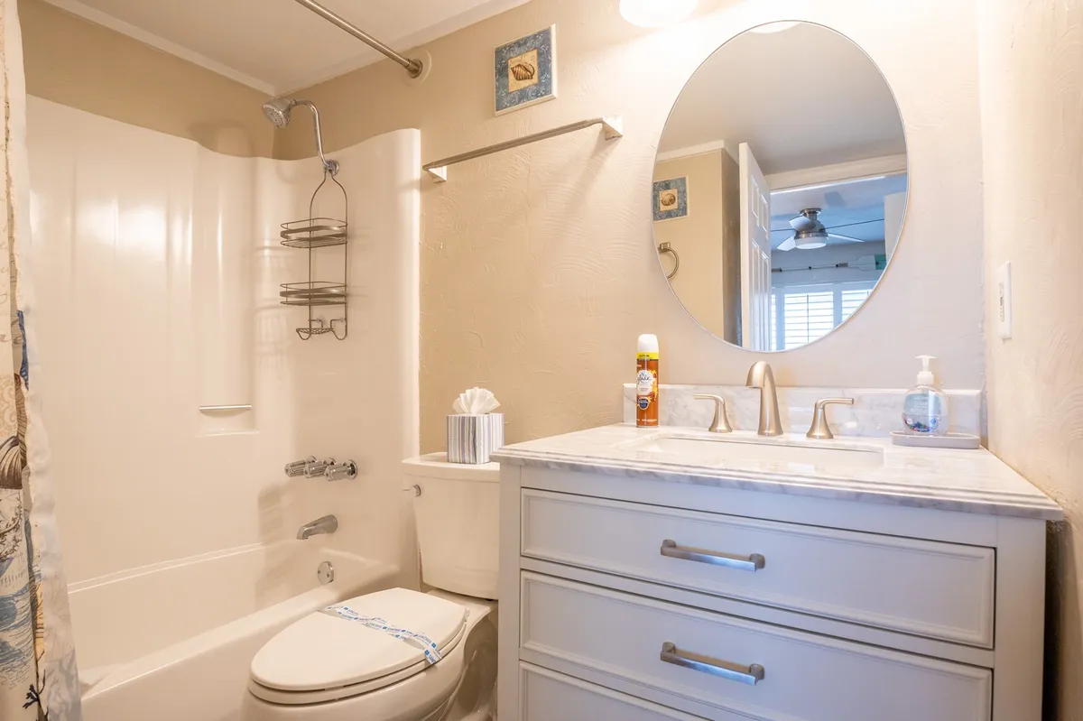 A modern bathroom space featuring a round mirror, sleek marble countertop, and colorful wall art, evoking a fresh and relaxing mood. The layout suggests a space ideal for morning routines or refreshing showers after a day out.