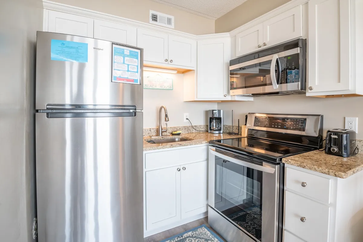 This image features a modern, functional kitchen with a stainless steel refrigerator, granite countertop, oven, microwave, and kitchen sink. The layout is compact, making all appliances easily accessible and ideal for quick meal preparation.