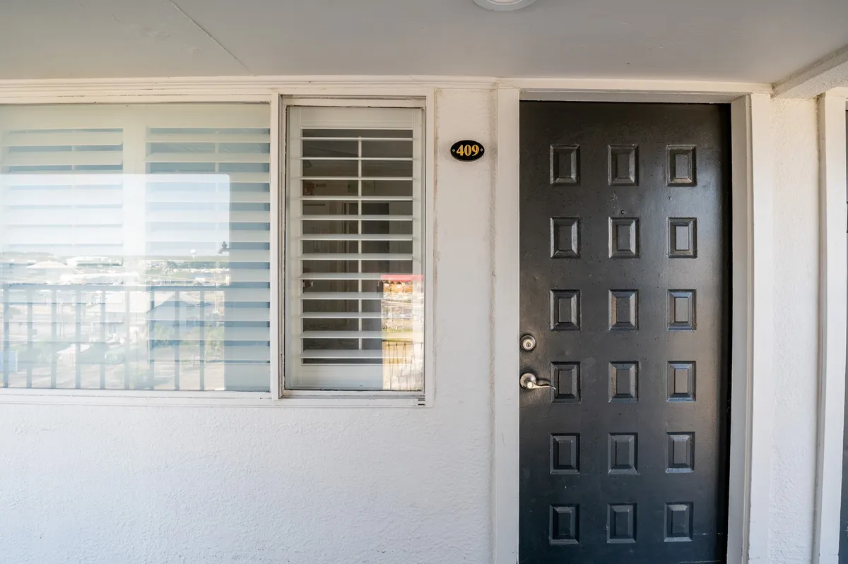 A welcoming view of the unit's entrance, featuring a black door with the room number '409' and a window with blinds. This image represents the first impression guests receive upon arrival and hints at the secure, well-maintained environment.