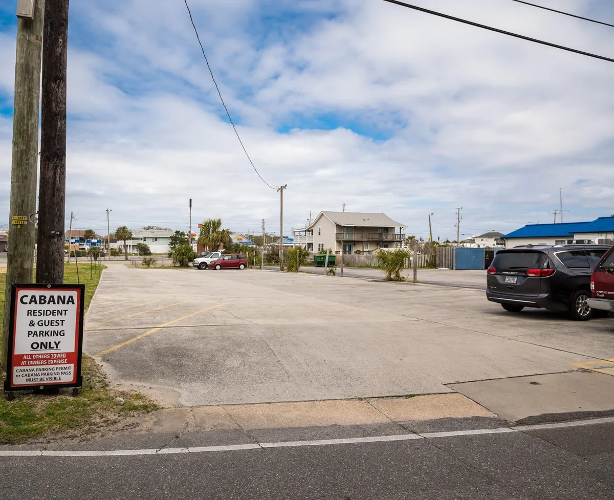 This exterior scene showcases a clearly marked parking area with a visible sign, several parked cars, and surrounding buildings. The atmosphere is relaxed, and the setting offers convenient access to local attractions and beach amenities.